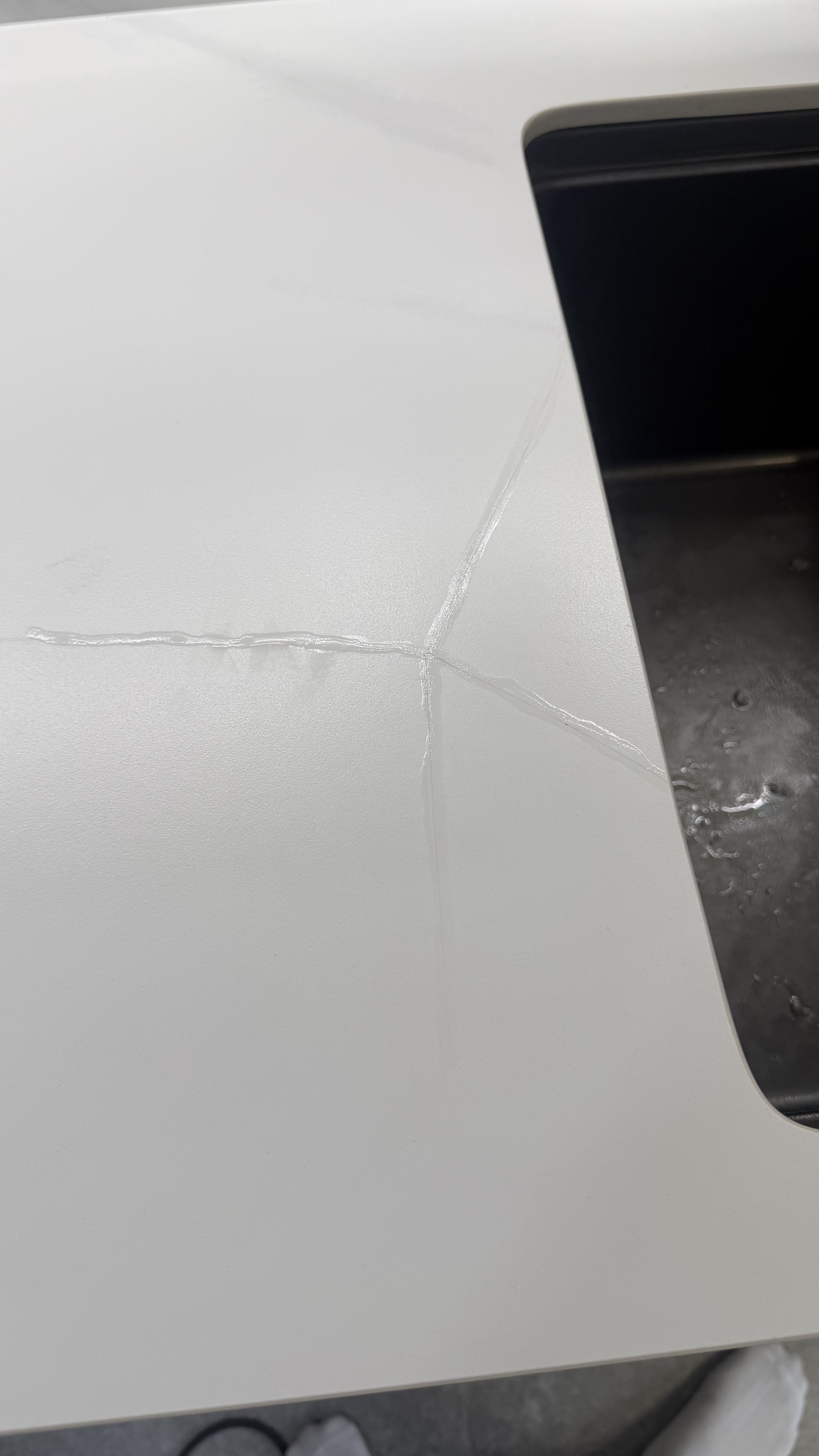 White Countertop Crack Repair — Before: Visible crack lines beside the sink opening before finishing.
